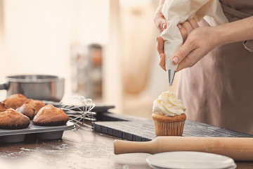 Woman decorating tasty cupcake with cream at table