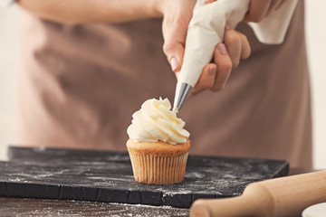 Woman decorating tasty cupcake with cream at table