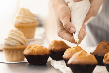 Woman decorating tasty cupcakes with cream at table