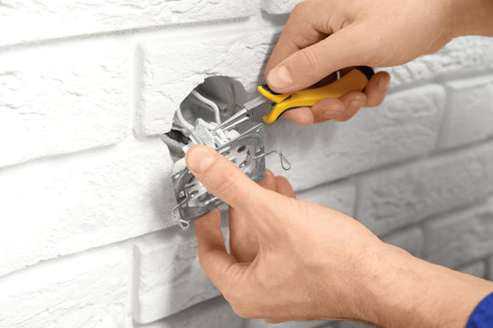 Electrician repairing socket on brick wall