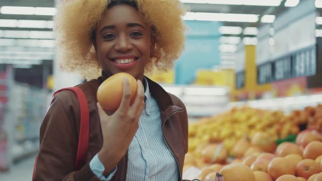 Portrait african american woman chooses grapefruit look at camera in supermarket food shopping fruit black working smiling family buying fresh grocery market mixed customers slow motion close up