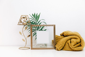 Minimal Mock up wooden frame with green tropical leaves and trendy warm sweater. Nordic decorations, Scandinavian style interior