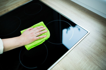 Young woman hands cleaning a modern black induction hob by a rag, housework