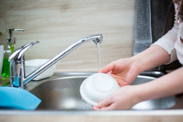 Young woman hands cleaning some dirty dishes by sponge and detergent