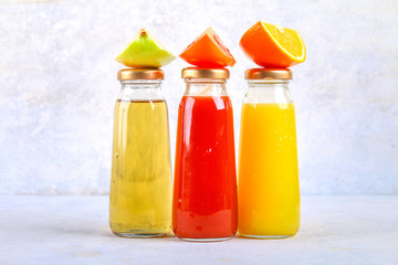 Bottles with fresh orange, apple, tomato juice on a gray concrete table. Lobules Fruits and vegetables around. Top view. Flat Lay.