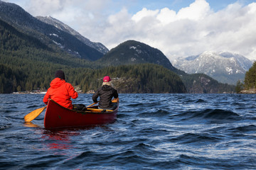 Couple friends on a wooden canoe are paddling in an inlet surrounded by Canadian mountains. Taken in Indian Arm, near Deep Cove, North Vancouver, British Columbia, Canada.