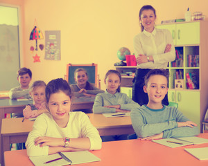 Smiling children sitting at lesson in classroom with teacher