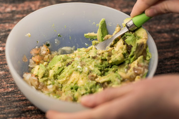 Cooking traditional latin american mexican sauce guacamole in a bowl with avocado, making guacamole in the kitchen, guacamole recipe