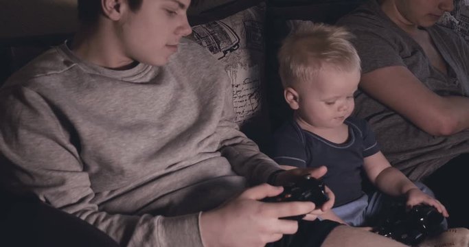 Guys and baby boy play video game console, have fun, laugh, hold joystick.