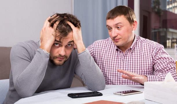 Friend calming distressed guy at home table