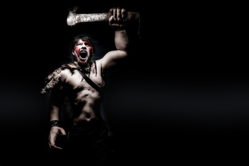 Fototapeta na wymiar Painted image of man in war paint, with an ax in his hand, a warrior brandishing an ax furiously screaming, barbarian of ancient times, Viking and savage.
