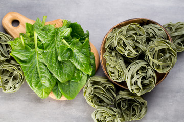 Fresh spinach with green pasta on a gray background.