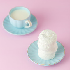 Pastel pink square banner with white zephyr on blue plate and cup of milk.