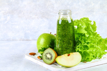 Green smoothies from parsley, salad, kiwi, apple in a bottle on a gray concrete table.
