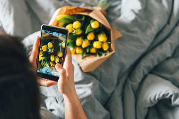 woman take picture of bouquet of yellow tulips. romantic surprise in bed