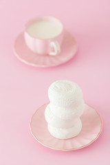 White zephyr dessrt on pink plate, cup of coffee with milk on pastel pink background. Beautiful sweets. Vertical banner, greeting card for birthday, wedding. Close up photography. Selective focus