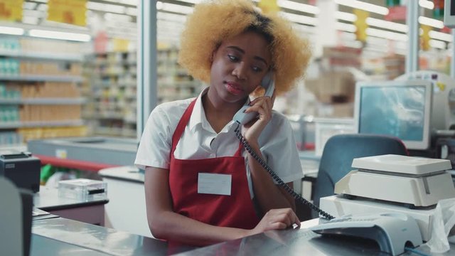 african american woman blond hair works at supermarket cash desk talk on phone look camera smile girl fruit technology grocery market store black retail indoors consumer vegetables fresh slow motion