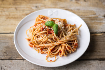 Homemade Italian pasta spaghetti with tomato sauce, fresh herbs and grated parmesan cheese on wooden rustic table
