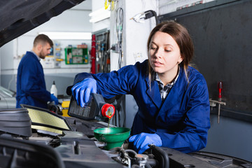 Young woman master is replacing the oil in the car in workshop.
