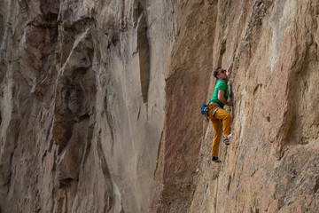 Adventurous man is rock climbing on the side of a steep cliff during a cloudy winter evening. Taken in Smith Rock, Oregon, North America.