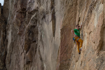 Adventurous man is rock climbing on the side of a steep cliff during a cloudy winter evening. Taken in Smith Rock, Oregon, North America.