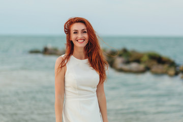 Portrait of happy redhead woman on the beach with flying hair in the wind