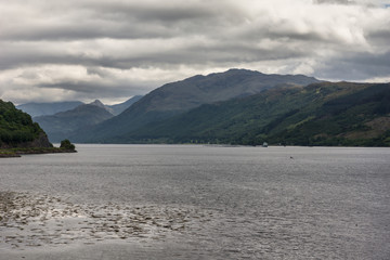 Dornie, Scotland - June 10, 2012: Confluence of Loch Duich, Loch Long and Loch Alsh at site of Eilean Donan Castl under rain-heavy cloudscape. Gray waters and dark mountains on the shores. 