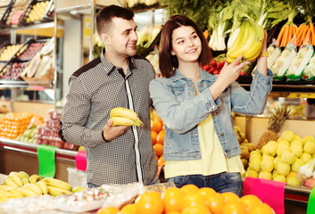 Obraz premium smiling couple choosing fruits in grocery shop