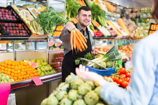 friendly male shopping assistant helping customer to buy fruit and vegetables in grocery shop