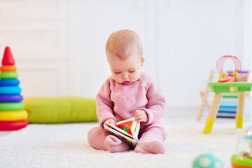 cute little baby girl sitting on the carpet among the development toys, with her first book
