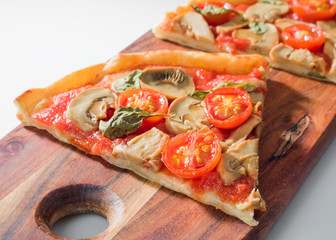 serving of mushroom and tomato pizza served on wooden board