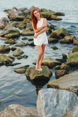 Pretty redhead woman stand alone on the rocks near the ocean
