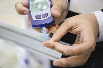 Glucometer - medical device. Man checks blood sugar level test by blood from finger, diabetic disease