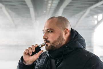 Vape man. Young guy vaping electronic cigarette or vape pen at urban background, modern lifestyle