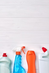 Set of bottles with cleaning liquid. House cleaning products on white wooden background and copy space, top view.
