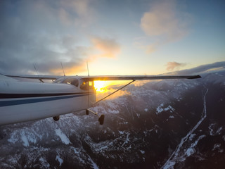 Small airplane flying overtop of the beautiful Canadian Mountain Landscape during a vibrant sunset. Taken North of Vancouver, British Columbia, Canada.