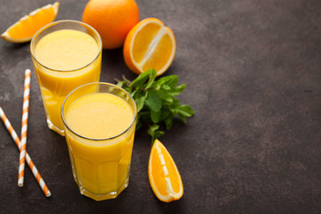 Two glasses of freshly squeezed orange juice and mint on a dark brown background. Top view with copy space