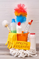 Orange bucket with bottles of cleaning liquids. Bucket with cleaning items on wooden background....