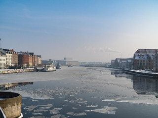 River/harbor in city with ice floes, blue sky and colored buildings