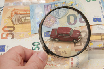 billetes de euro y coche mirado con lupa