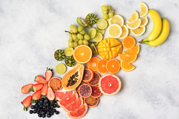 Above view of healthy fruits in rainbow colours, strawberries, mango, grapes, bananas, grapefruit on the off white table, copy space for text, selective focus