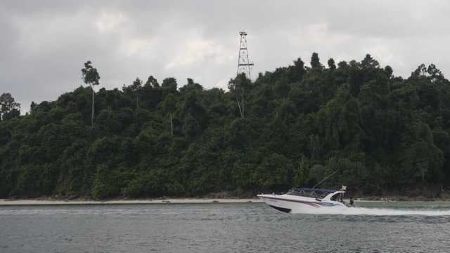 Speed motor boat navigating in bay against background with tropical rainforest.