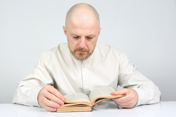 bald, bearded man in bright clothes reading a book of the Bible.