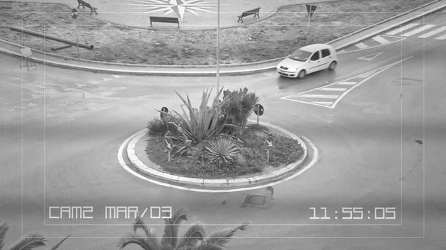 A CCTV security camera recording: a roundabout with some cars passing by.
