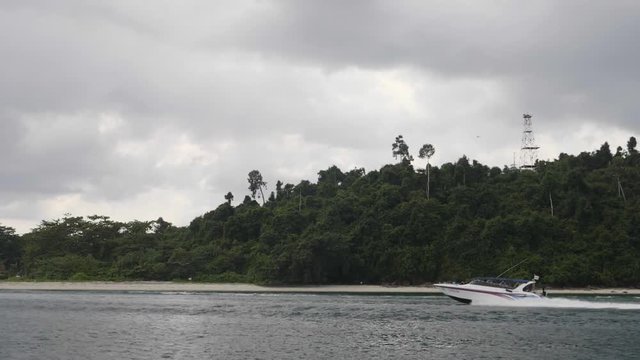 Speed motor boat navigating in bay against background with tropical rainforest.