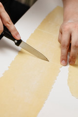 Man's hands cutting thinly rolled layer of Italian pasta dough for making meat or spinach and ricotta filled Ravioli at home