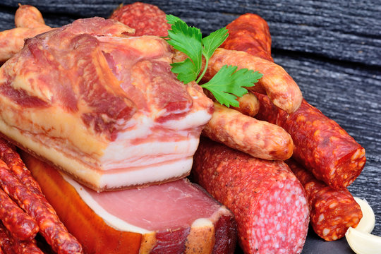 Bacon with sausages and prosciutto crudo and salami on a wood background