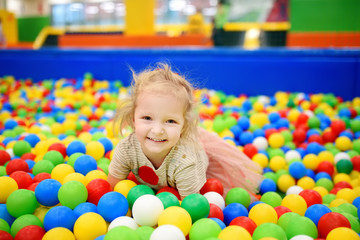 Fototapeta na wymiar Curly little girl having fun in ball pit with colorful balls