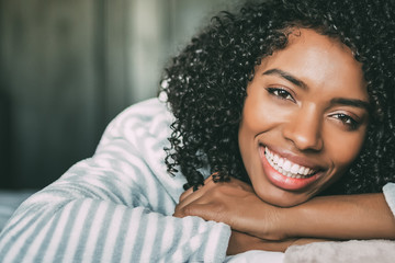 close up of a pretty black woman with curly hair smiling and lying on bed looking at the camera