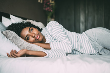 close up of a pretty black woman with curly hair smiling and lying on bed looking away